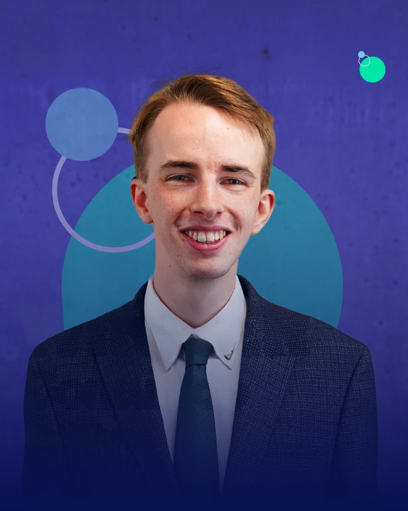 Paul Wilson in a suit, smiling, against a coloured background.